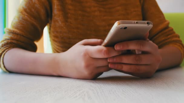 Flicka i gul Tröja sitter på ett café och något är att skriva på en smartphone — Stockvideo