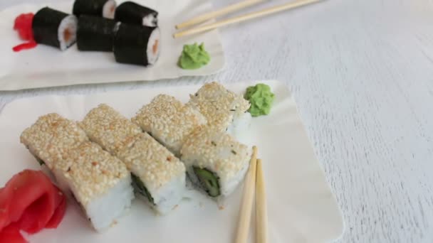 Delizioso sushi-maki con salmone e sushi con pesce, zenzero rosa, wasabi verde su un piatto e salsa di soia su un bellissimo sfondo bianco elegante — Video Stock