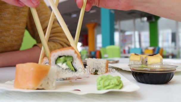 Menina e um cara estão sentados em um bar de sushi e tomar com paus de sushi de madeira — Vídeo de Stock