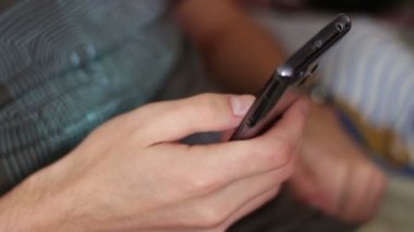Genç bir akıllı telefon tutarak ve bir ileti yazdırma kanepede yatıyor