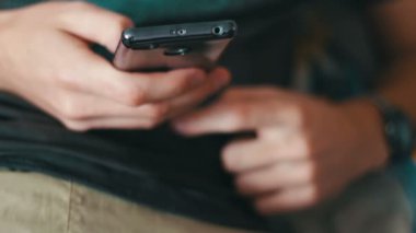 adam bir T-shirt ve şort kanepede yatıyor ve bir akıllı telefon tutuyor