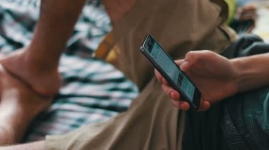 adam bir T-shirt ve şort kanepede yatıyor ve bir akıllı telefon tutuyor