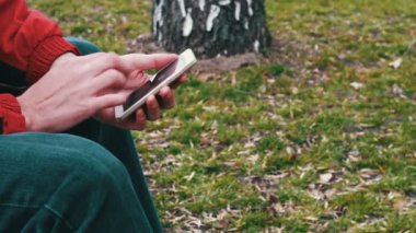 Yalnız bir kırmızı ceket parkta oturan ve bir şey Smartphone'da yazarak