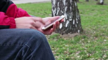 Sokakta, parkta, açık beyaz telefon ile genç adam oturur