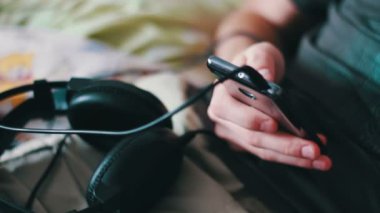 adam bir T-shirt ve şort kanepede yatıyor ve bir akıllı telefon tutuyor