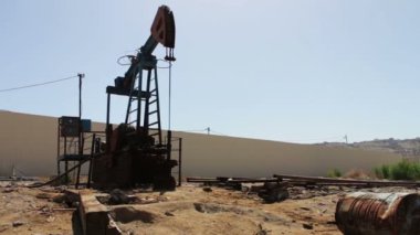 Petrol pumpjacks çalışma petrol alanında Bakü, Azerbaijan.Silhouette çalışma yağ pompası ve bir eski paslı demir varil yakınındaki bir zemin üzerine mavi gökyüzü ve bulutlar