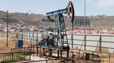 Yağ pompası ve bir eski paslı demir varil yakınındaki bir zemin üzerine mavi gökyüzü ve bulutlar çalışma siluet. Yağ pumpjacks bir çalışma petrol alanında, Bakü, Azerbaycan.