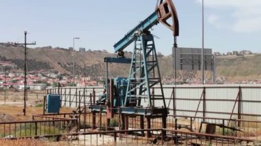 Yağ pompası ve bir eski paslı demir varil yakınındaki bir zemin üzerine mavi gökyüzü ve bulutlar çalışma siluet. Yağ pumpjacks bir çalışma petrol alanında, Bakü, Azerbaycan.
