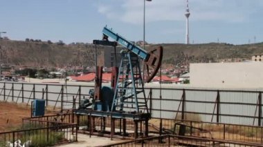 Yağ pompası ve bir eski paslı demir varil yakınındaki bir zemin üzerine mavi gökyüzü ve bulutlar çalışma siluet. Yağ pumpjacks bir çalışma petrol alanında, Bakü, Azerbaycan.