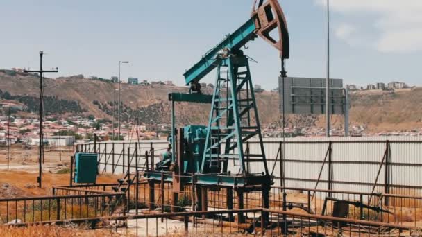 Silhouette einer funktionierenden Ölpumpe und eines alten rostigen Eisenfasses in der Nähe vor blauem Himmel und Wolken. Ölpumpjacken in einem arbeitenden Ölfeld in Baku, Azerbaijan. — Stockvideo