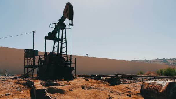 Нефтяные насосы на действующем нефтяном месторождении в Баку, Азербайджан. Силуэт работающего нефтяного насоса и старая ржавая железная бочка рядом на фоне голубого неба и облаков — стоковое видео