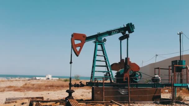 Silueta de la bomba de aceite de trabajo y un viejo barril de hierro oxidado cerca sobre un fondo de cielo azul y nublas.Petroleras en un campo petrolero de trabajo en Bakú, Azerbaiyán . — Vídeo de stock