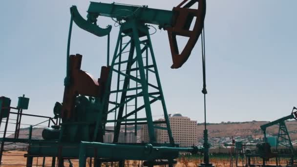 Silhouette einer funktionierenden Ölpumpe und eines alten rostigen Eisenfasses in der Nähe vor blauem Himmel und Wolken. Ölpumpjacken in einem arbeitenden Ölfeld in Baku, Azerbaijan. — Stockvideo