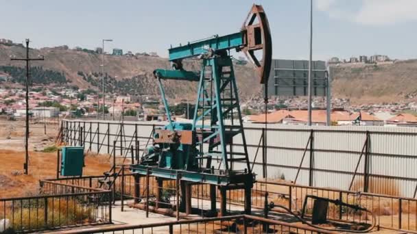 Silhouette einer funktionierenden Ölpumpe und eines alten rostigen Eisenfasses in der Nähe vor blauem Himmel und Wolken. Ölpumpjacken in einem arbeitenden Ölfeld in Baku, Azerbaijan. — Stockvideo