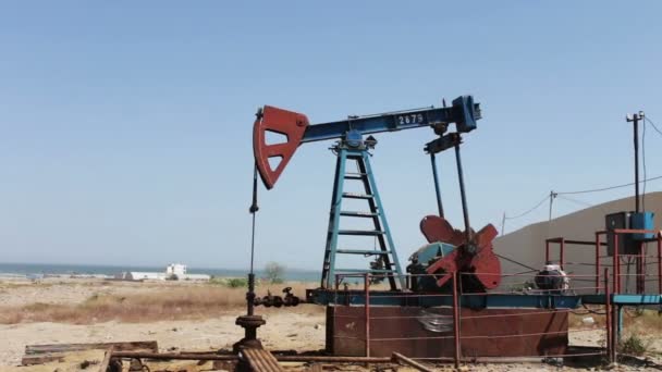 Silhouette d'une pompe à huile en état de marche et d'un vieux baril de fer rouillé près d'un fond de ciel bleu et de nuages. . — Video