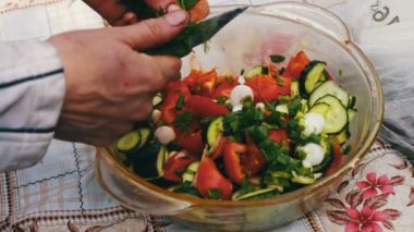 Bahçedeki masada domates, armut ve yeşillik salatası var. El salata keser. Sağlıklı bir salata sebze. Evin dışında piknik.