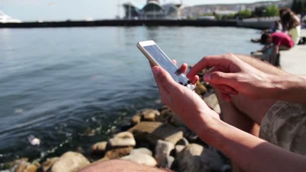Eller genç bir adam bir şey bir smartphone cep telefonu ile Hazar denizin dalgaları zemin karşı yazın — Stok video