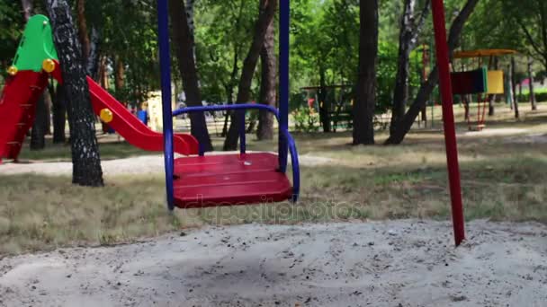 Red childrens swing swings from side to side in summer — Stock Video