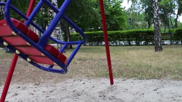 Red childrens swing swings from side to side in summer — Stock Video