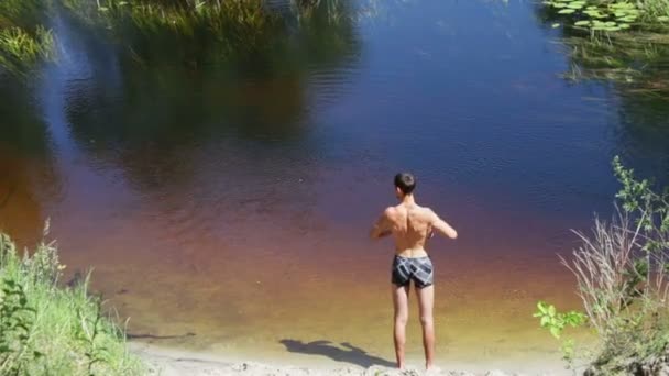 Hombre delgado haciendo ejercicios en la orilla del río salvaje — Vídeos de Stock