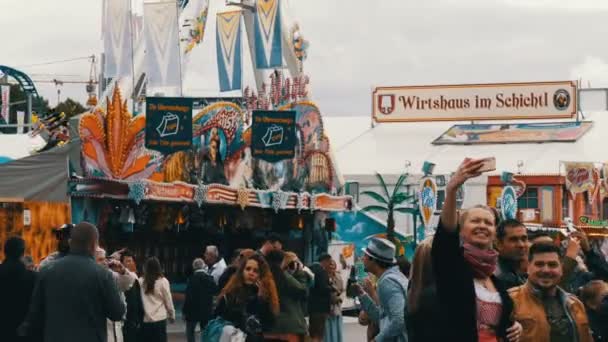 September 17, 2017 - Munich, Germany: The largest beer festival Oktoberfest. People in national Bavarian suits Lederhose and Dirdln walk around amusement rides at Theresienwiese, girl makes selfie — Stock Video