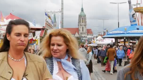 17 de septiembre de 2017 - Munich, Alemania: una multitud de personas vestidas con disfraces nacionales bávaros caminan a lo largo del Oktoberfest pasando por atracciones de entretenimiento y tiendas de campaña con comida y dulces — Vídeo de stock