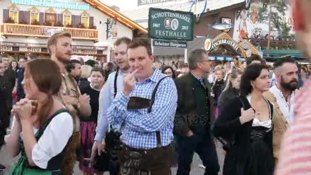 17 de septiembre de 2017 - Oktoberfest, Múnich, Alemania: Hermosos jóvenes entre la multitud de transeúntes esperando a alguien en un festival de cerveza un tipo mostrando un gesto indecente a la cámara — Vídeos de Stock