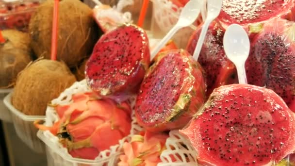 Pitaya juteux mûr de couleur rouge-rose à côté des noix de coco sur le comptoir du marché aux fruits en Espagne — Video