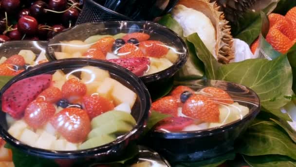 Mezcla de diferentes frutas de fresa mango kiwi pitaia y otras en un plato de plástico en el mostrador del mercado de frutas en Barcelona, España — Vídeos de Stock