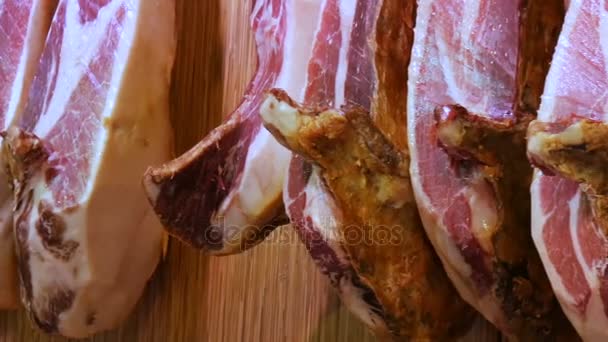 Сушеные свиные бёдра висят на столе мясного рынка. Испанское национальное блюдо из ветчины или хамона с полосками жира, рынок Ла-Бокерия, Испания — стоковое видео