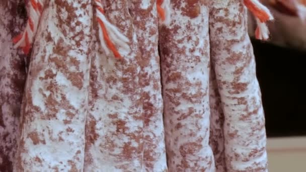 Deliciosas salsichas de salame fresco penduradas no balcão do mercado de açougueiro de carne de perto — Vídeo de Stock