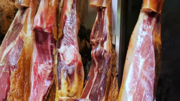 Coxas de porco secas penduradas no balcão do mercado de carne. Prato nacional espanhol de presunto ou jamon com listras de gordura — Vídeo de Stock
