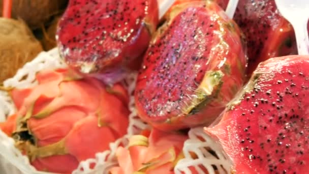 Спелые сочные красно-розовый цвет pitaya рядом с кокосами на столе фруктового рынка в Испании — стоковое видео