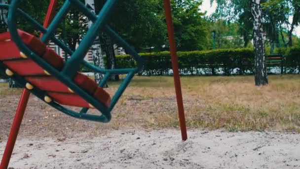 Red childrens swing swings from side to side in summer — Stock Video