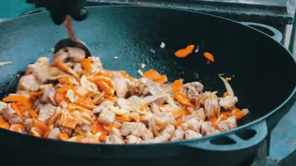 Самый вкусный узбекский плов с морковью, рисом и мясом варится в огромной ванне на фестивальном фудкорте — стоковое видео