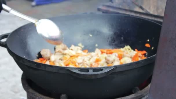 Carne saborosa e suculenta é frita com legumes em uma tigela enorme e misturada com uma colher em um festival de comida de rua. — Vídeo de Stock
