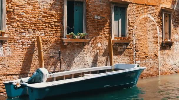 VENISE, ITALIE, 7 SEPTEMBRE 2017 : Bateau à moteur se dresse sur un canal vénitien sous un beau mur de briques vintage et des fenêtres avec des fleurs dans des pots sur les appuis des fenêtres — Video