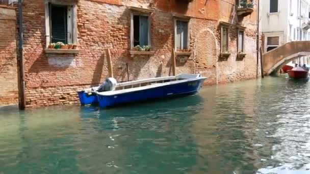 VENECIA, ITALIA, 7 DE SEPTIEMBRE DE 2017: una acogedora pared de una casa de ladrillo veneciano junto a un barco estacionado y pasando por un canal otro barco con gente — Vídeos de Stock