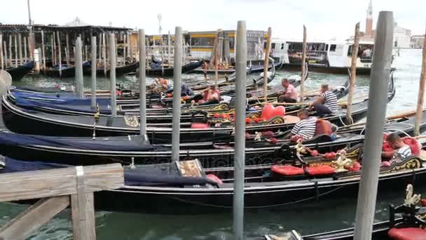 VENICE, ITALY, SEPTEMBER 7, 2017: Many beautiful gondolas that stand in a row on the grand canal, in which sit gondoliers and past the crowds of tourists — Stock Video