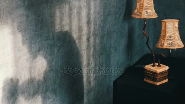クッキーを食べて、マグカップからお茶を飲むビンテージ黄色ランプの横にあるゴシック様式の暗い部屋で猫背の恐ろしい影。幽霊やハロウィーンの魔女. — ストック動画