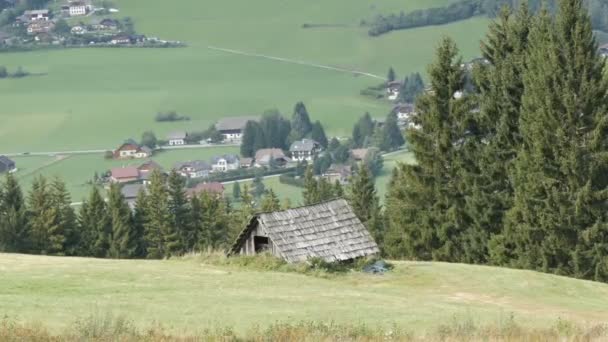 Útulný velmi starý retro dřevěný dům v rakouských Alpách na kopci s trávou na pozadí nových moderních domů, staré zemědělské zemi dřevěný dům v obci — Stock video