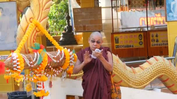 Pattaya, thailand - 18. Dezember 2017: Buddhistischer Mönch in rotem Gewand hält ein Smartphone in der Hand, Touristen kommen vorbei. Hügel des großen Buddha — Stockvideo