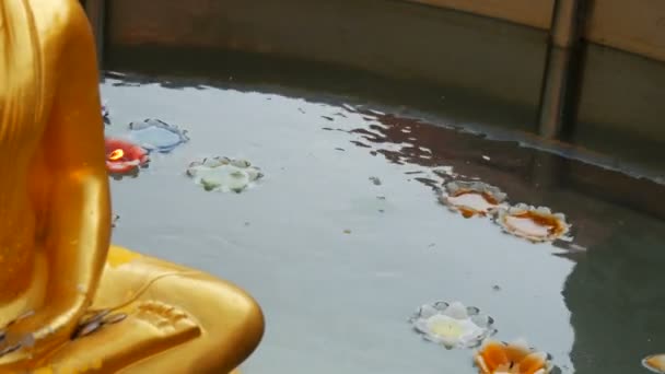 Aranyozott Buddha-szobor, amely úszó körül sokszínű viasz gyertya, az alakja egy lotus — Stock videók