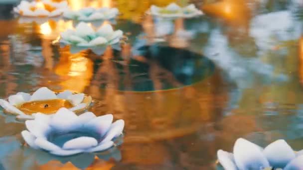 Mooie gouden weerspiegeling van het Boeddhabeeld in een water, waarop diverse wax kaarsen in de vorm van lotus float — Stockvideo