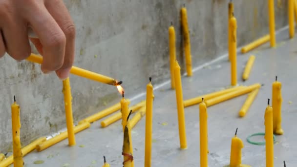 Eine dünne gelbe Wachskerze entzündet eine weitere Kerze mit ihrer Flamme. viele dünne gelbe Wachskerzen — Stockvideo