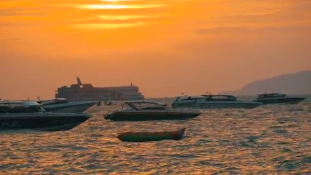 PATTAYA, TAILANDIA - 25 DE DICIEMBRE DE 2017: Una pintoresca puesta de sol roja en la orilla del mar contra el telón de fondo de las montañas. Las olas del mar golpean contra la costa por la noche. Barcos de recreo en el mar — Vídeo de stock