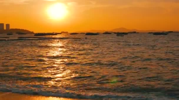 PATTAYA, TAILANDIA - 25 DE DICIEMBRE DE 2017: Una pintoresca puesta de sol roja en la orilla del mar contra el telón de fondo de las montañas. Las olas del mar golpean contra la costa por la noche. Barcos de recreo en el mar — Vídeos de Stock