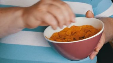 Şişko, tembel adam bir sandalyede oturan cips yiyor. Çizgili bir T-shirt altında bir adam büyük bir göbek. Fast food, değil sağlıklı gıda