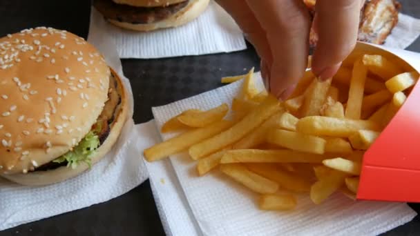 Handen van een vrouw nemen Franse frietjes. Hamburgers, kippenvleugeltjes, Franse frietjes op dienblad in een fast food restaurant. Ongezonde voeding — Stockvideo