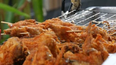 Sokak gıda Tayland. Kızarmış tavuk parçaları içinde meyilli. Satıcı sokakta bir egzotik yemek satıyor. Alıcı bir parça et yemek için özel maşa yardımıyla seçer